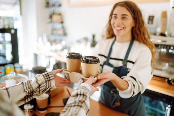 Smiling Barista Girl Giving Take Away Coffee Cups To A Customers.